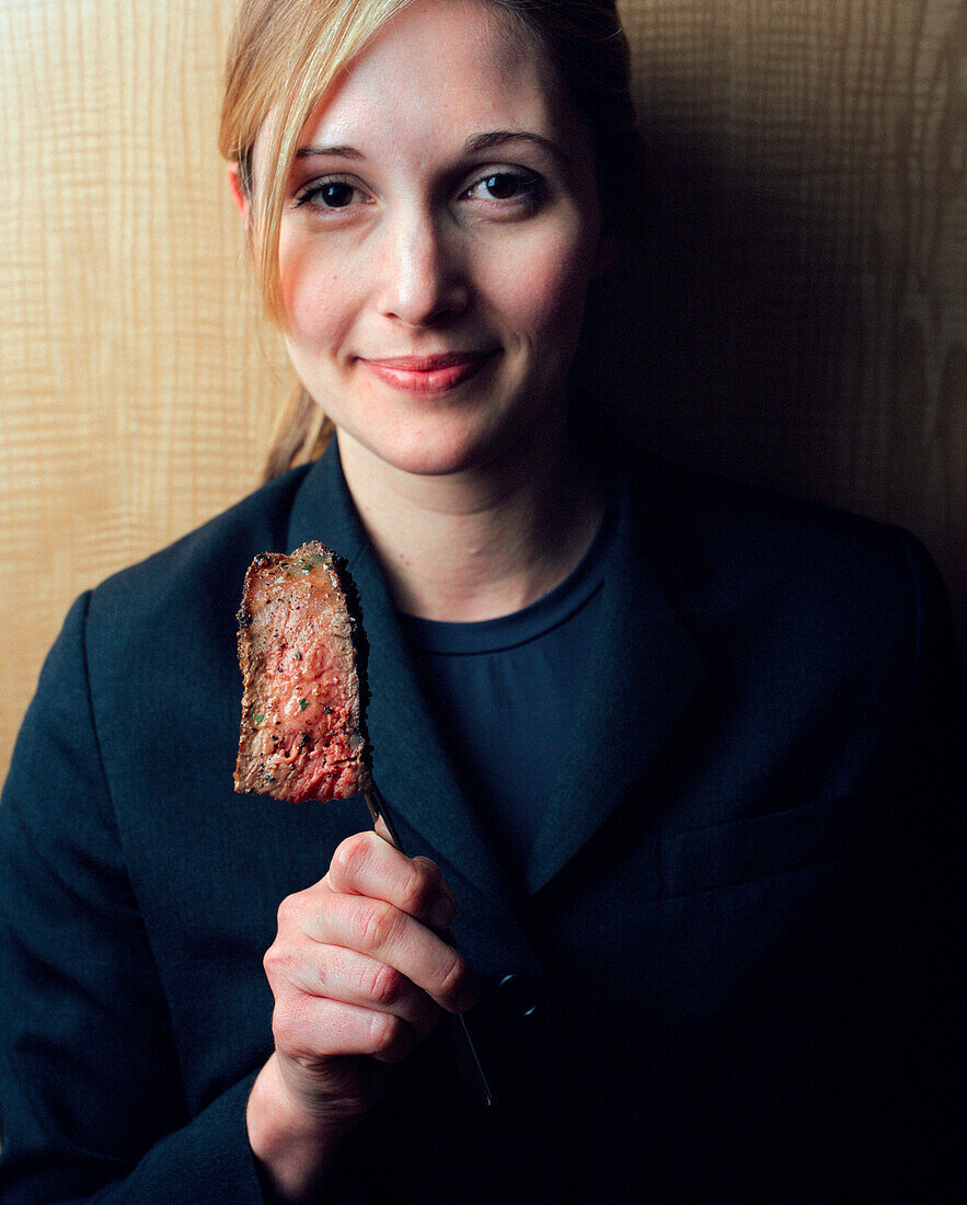 USA, California, Los Angeles, portrait of a young waitress holding a slice of steak on a fork at CUT Restaurant.