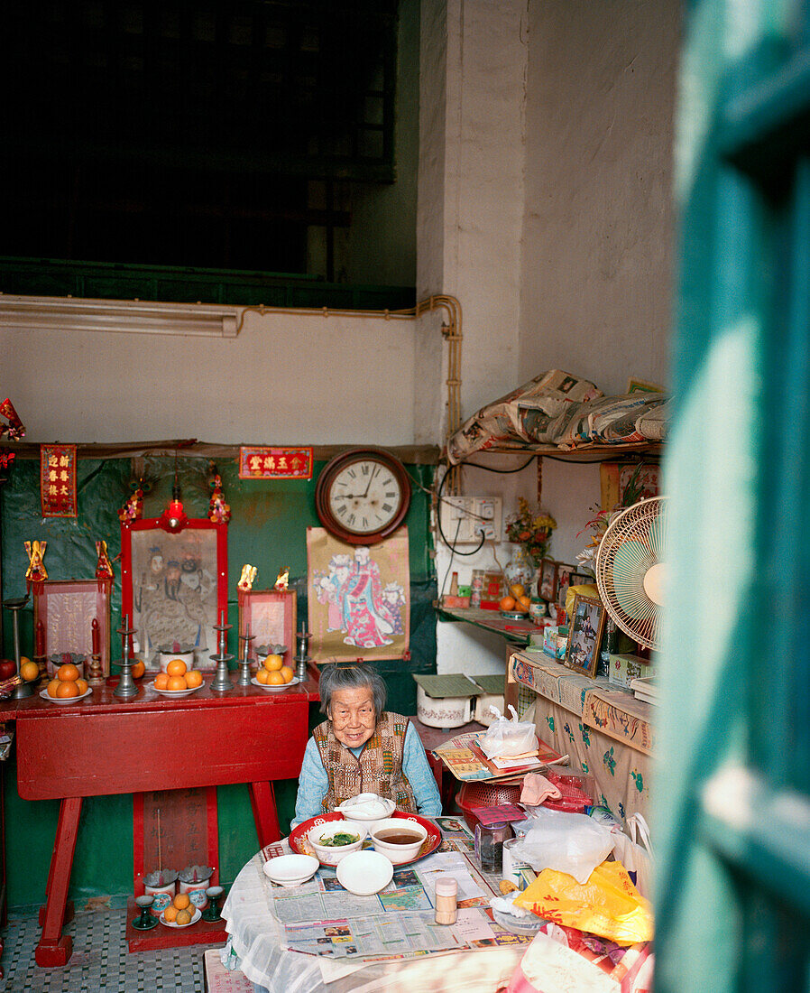 CHINA, Macau, Old Chinese woman dining at table in messy house