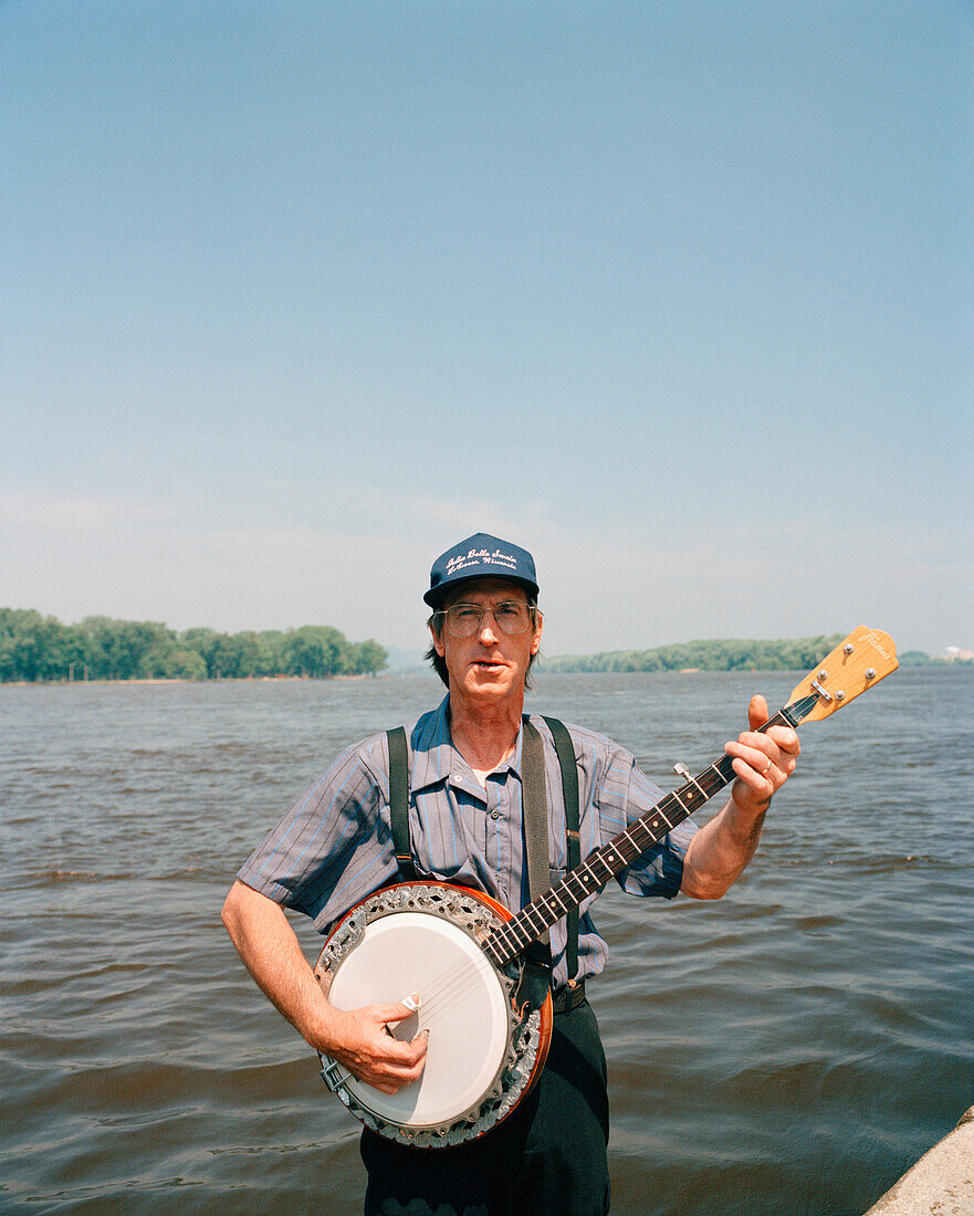 USA, Minessota, Lacrosse, portrait of mature man playing banjo against the Mississippi River.