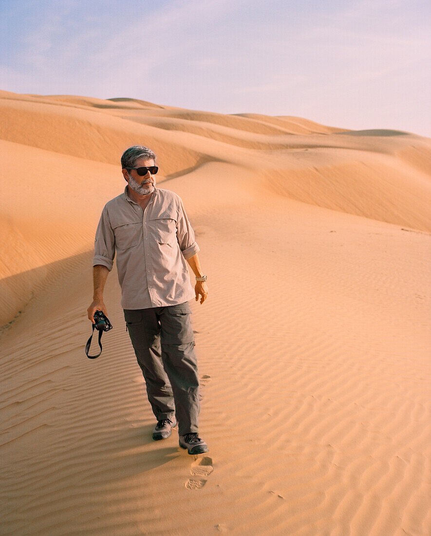OMAN, Muscat, mature man walking in desert, holding camera
