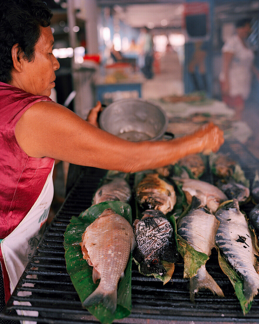 PERU, Amazon Rainforest, South America, Latin America, vendor grilling fishes on coal at the Bellavista Market.