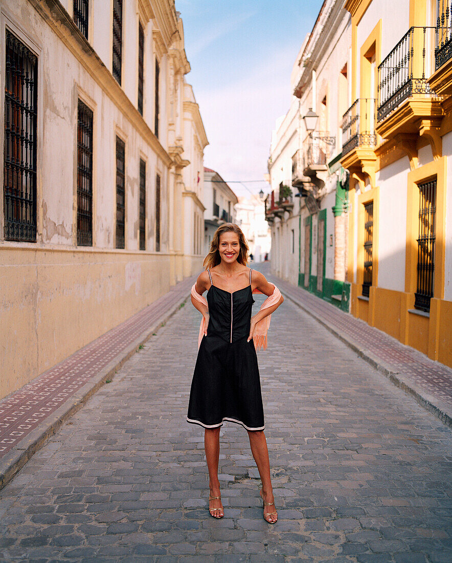 SPAIN, Andalusia, Tarifa, young woman standing on alley amid buildings, portrait