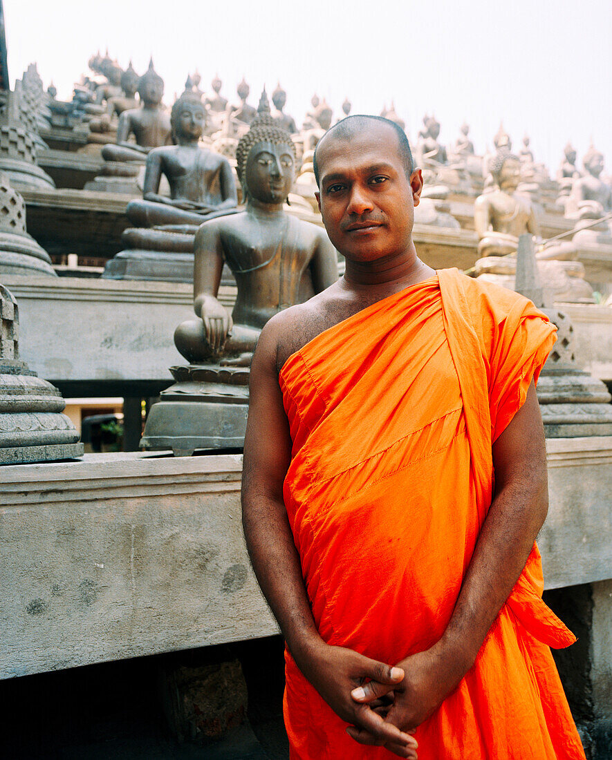 SRI LANKA, Asia, portrait of a monk with Buddha statues in the background