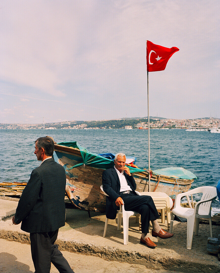 TURKEY, Istanbul, portrait of a fisherman sitting with Turkish flag beside it