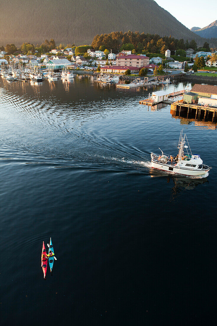 ALASKA, Sitka, kayakers take a rest in Sitka Harbor while a fishing boat passes by