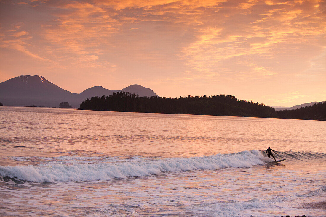 ALASKA, Sitka, a surfer catches waves created by the tidal shift, dormant volcano Mount Edgecumbe in the background, Halibut Cove, Sitka Sound
