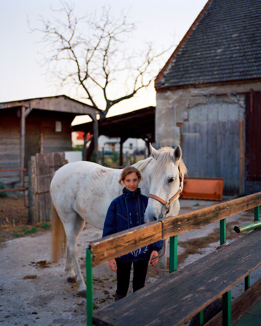 AUSTRIA, Podersdorf, a young girl Denise stands with her horse in front of her home, Burgenland