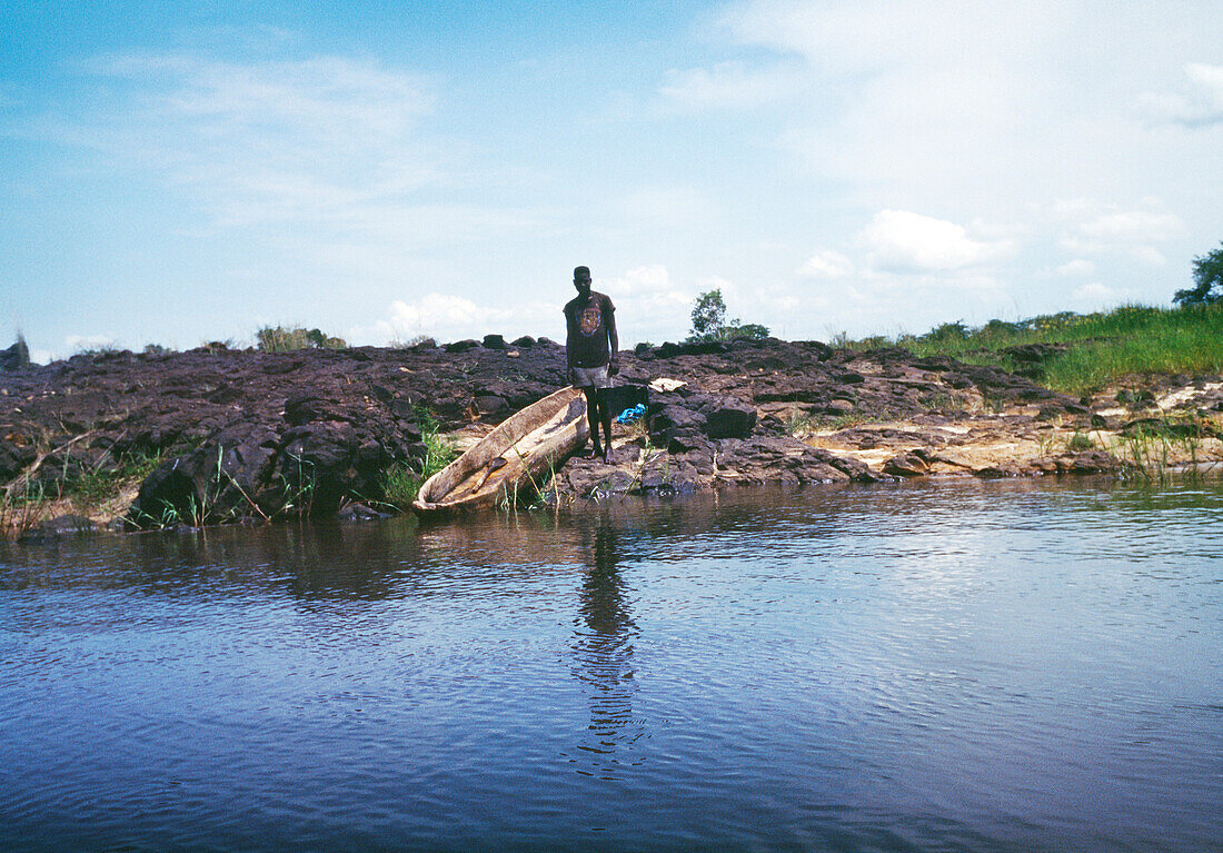 BOTSWANA, Africa, a lone man with his dugout canoe standing on the edge of the Zambezi River