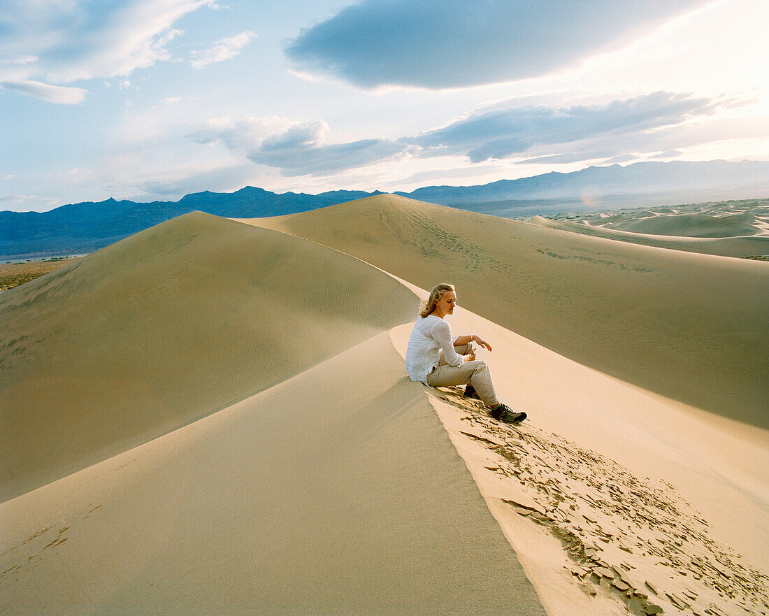 USA, California, young woman sitting on sand dune, Stovepipe Wells, Death Valley National Park