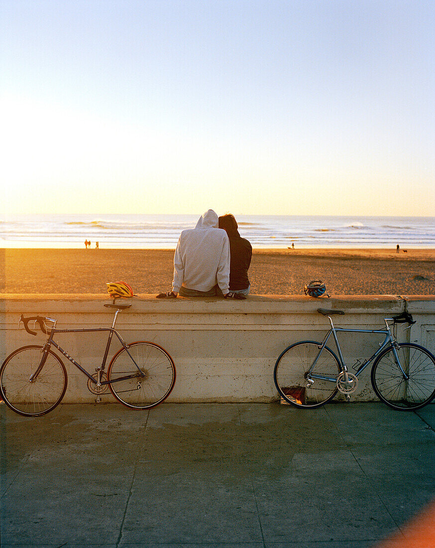 USA, San Francisco, a couple sit and watch the sunset at Ocean Beach