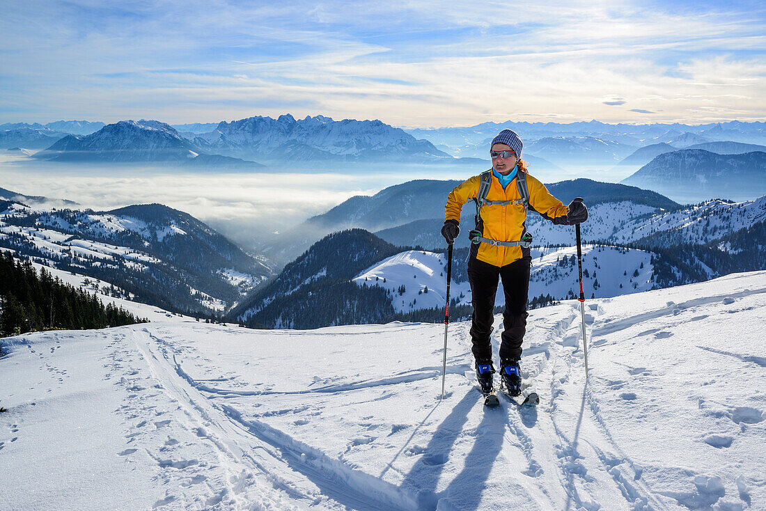 Female backcountry skier ascending to Grosser Traithen, Kaiser mountain range in background, Mangfall range, Bavarian Alps, Upper Bavaria, Bavaria, Germany