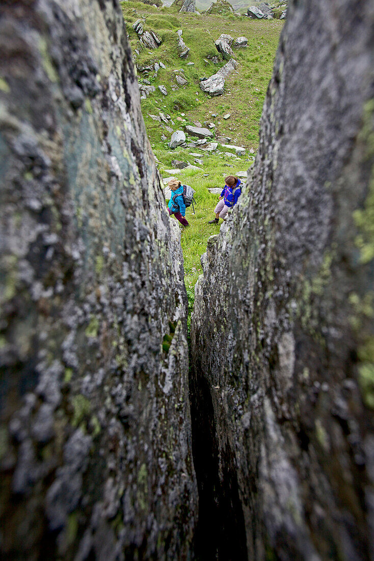 Two female hikers passing a rock crevice, Alpe-Adria-Trail, Nockberge, Carinthia, Austria