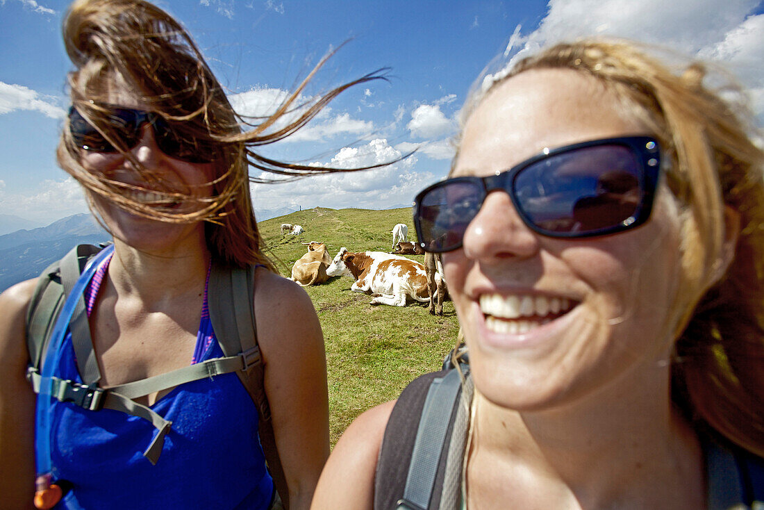 Zwei junge Frauen lachen, Herde Kühe im Hintergrund, Alpe-Adria-Trail, Nockberge, Kärnten, Österreich