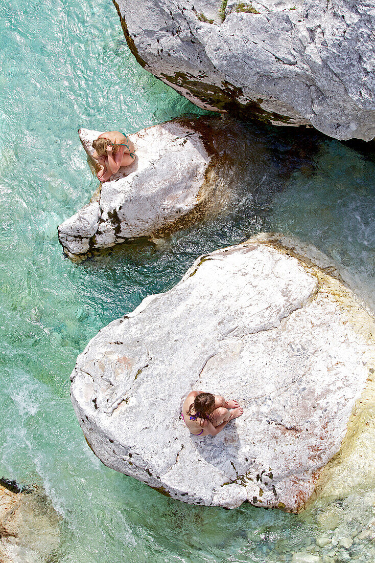 Two young women sitting on rocks in the river Soca, Alpe-Adria-Trail, Tolmin, Slovenia