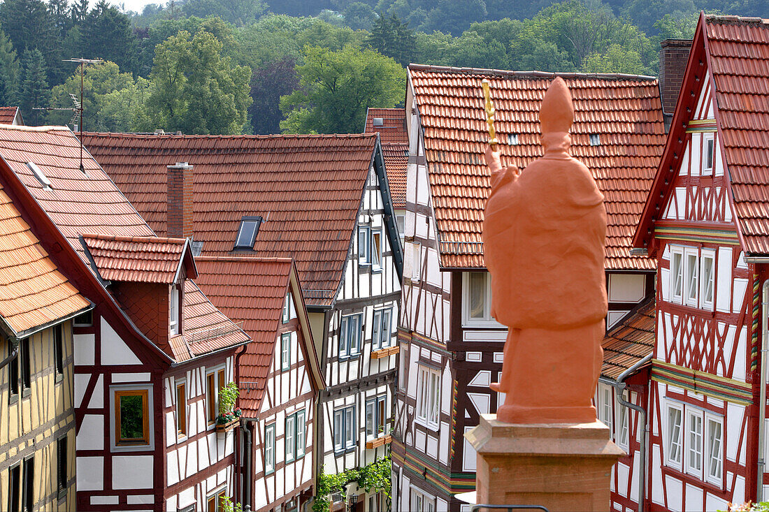 Bishop statue at the top of the church steps and view into Kirchgasse, a beautiful alley in the historic old town of Bad Orb, Spessart, Hesse, Germany