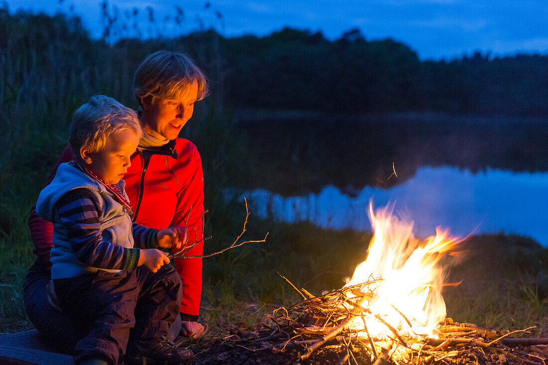 Mother and son (2 years) near a campfire at lakeside, near Blumenholz, Mecklenburg-Western Pomerania, Germany