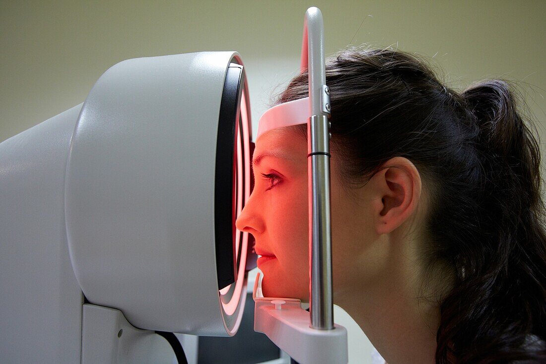 Augenuntersuchung Patientin, bei der eine Hornhauttopografie-Messung ihres Auges durchgeführt wird Das Gerät in der Mitte projiziert helle Ringe auf das Auge, die sich in seiner Oberfläche spiegeln Durch die Untersuchung der Reflexion kann ein genaues Modell der Form des Auges erstellt werden