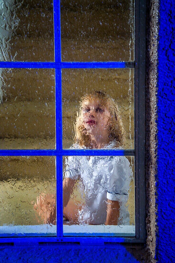 A five-year-old girl looks out her window on a rainy night in suburban Lake Forest, CA