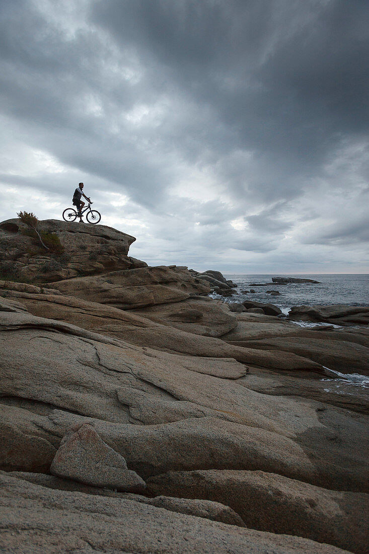Man sitting on bicycle on boulder