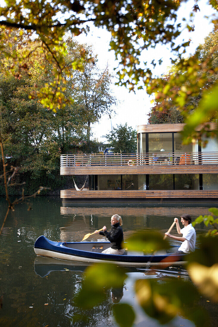 Couple canoeing on Eilbek canal, houseboat in background, Hamburg, Germany