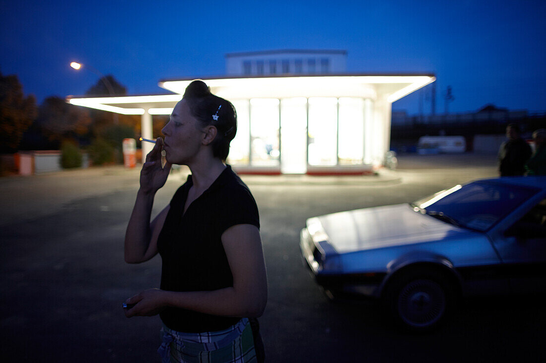 Woman smoking in front of the oldtimer gas-station Brandshof, listed building from 1953, ICE high speed train is above, Billhorner Roehrendamm 4, Hammerbrook, Hamburg, Germany
