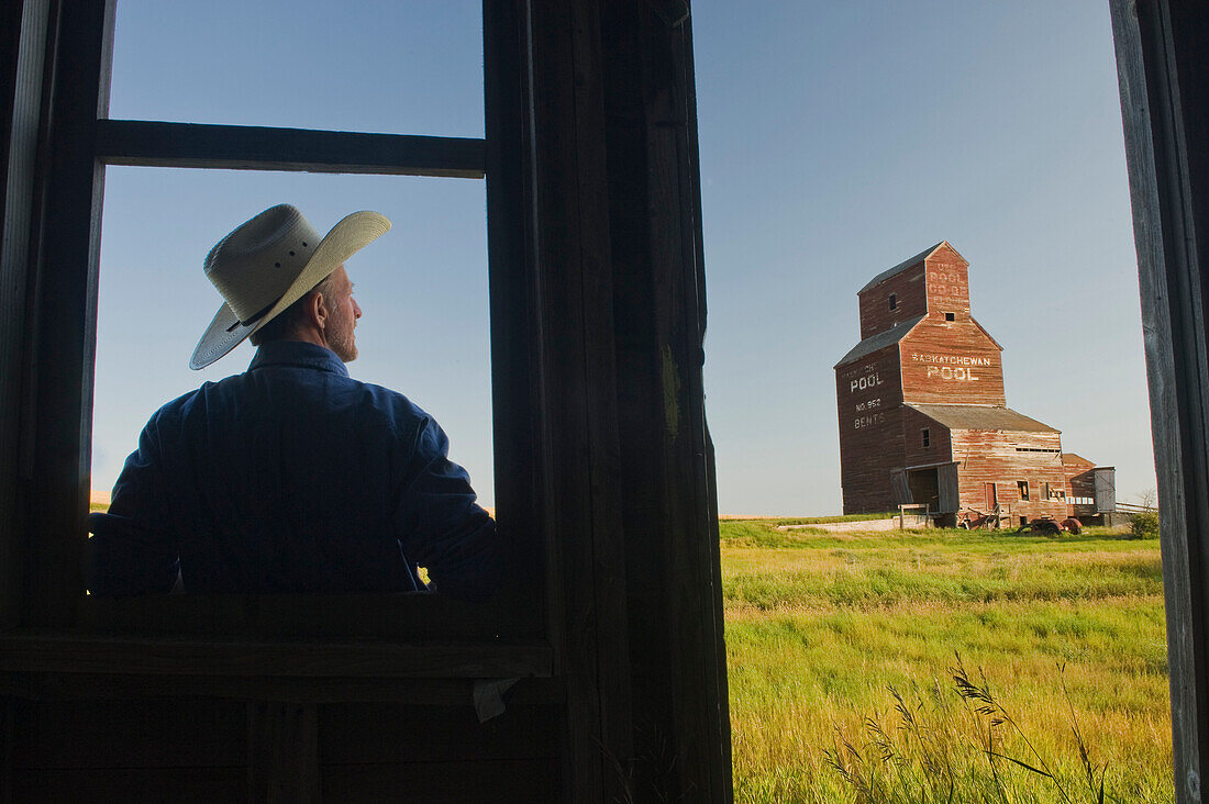 Farmer looking towards an abandoned grain elevator, in the ghost town of Bents, Saskatchewan