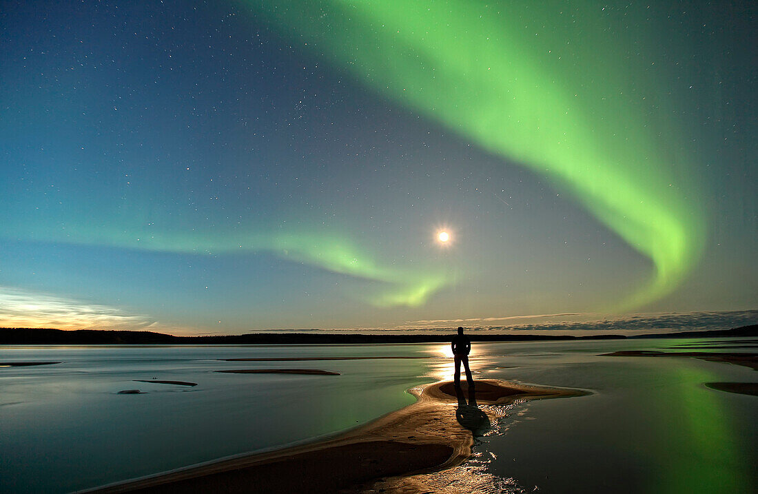 Person standing under an aurora borealis by the MacKenzie River, Fort Simpson, Northwest Territories, Canada