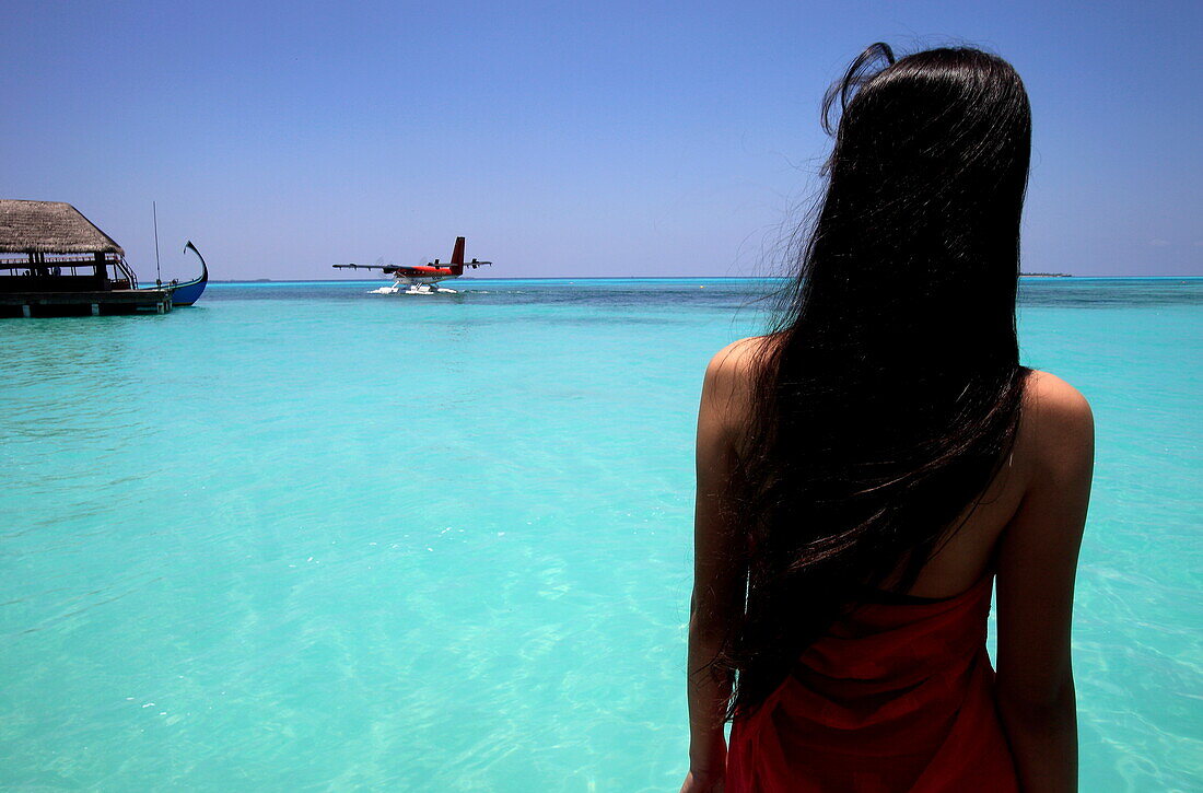 Republic of the Maldives, Lhaviyani Atoll,  Kanuhura Hotel, rear view of a woman looking at a seaplane