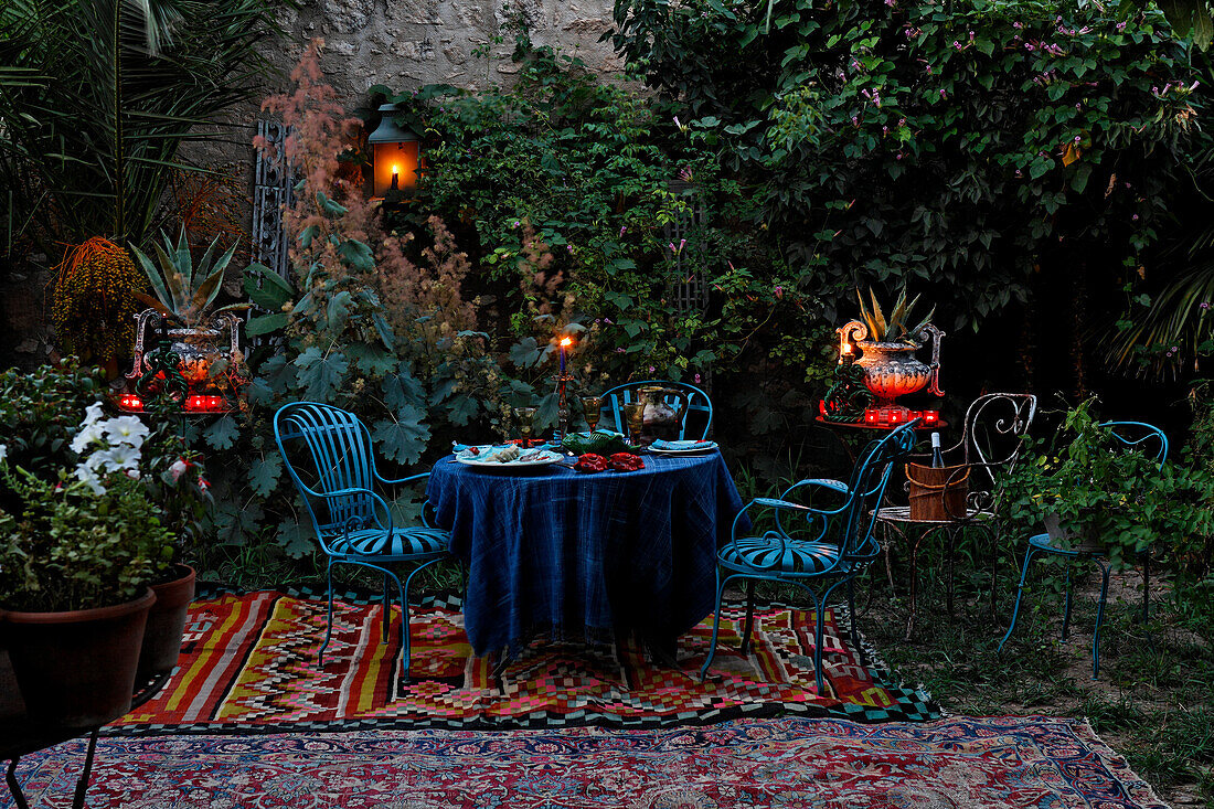 Romantic Ambiance, Wrought iron garden furniture with carpets and candle jars in a private garden at dusk