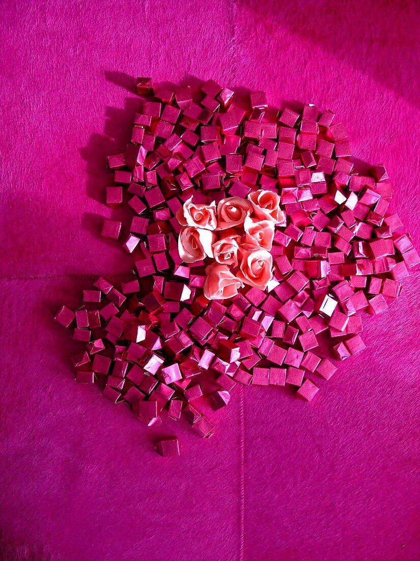 Chocolate candies wrapped pink papers with roses, in the shape of an heart