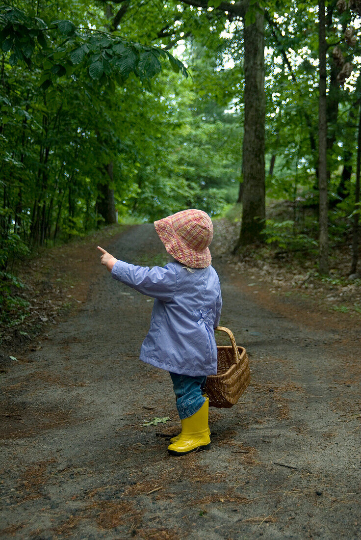 Little Girl in a Rain Coat and Rubber Boots with a Basket Pointing to Trees on a Trail, Lake Muskoka, Bracebridge, Ontario