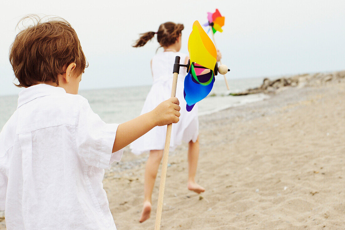 Brother and Sister Running along a Beach Holding Pinwheels, Toronto, Ontario