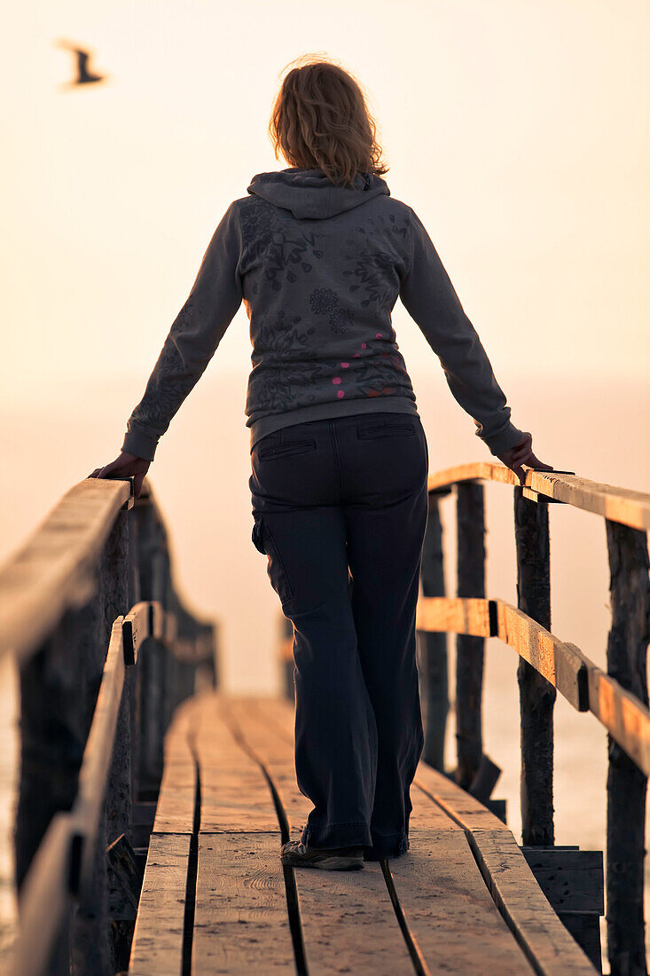 Woman on wooden pier at sunrise, seagull silhouette in distance, Lake Winnipeg, Matlock, Manitoba