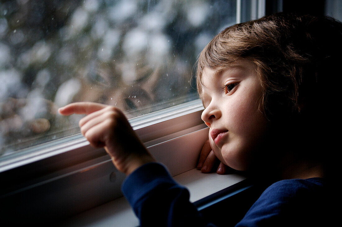 Young boy looking out a window and scratching the glass, Otterburn Park, Quebec