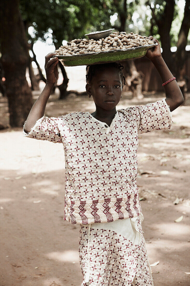 Mädchen trägt ein Tablett mit Erdnüssen auf dem Kopf zum Markt, Yanfolila, Sikasso, Mali