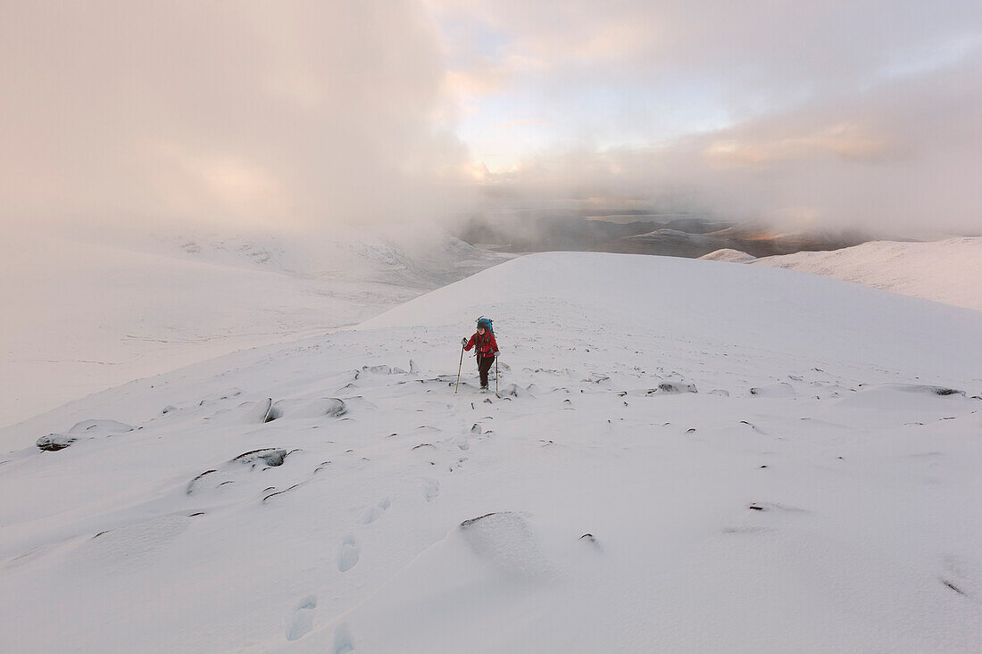 Junge Frau mit Rucksack wandert im Schnee auf einen Gipfel des An Teallach, Dundonnell, Northwest Highlands, Schottland, Großbritannien
