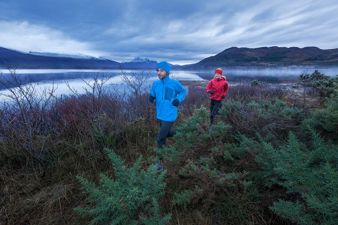 Young couple jogging along Loch Maree, Northwest Highlands in background, Scotland, United Kingdom