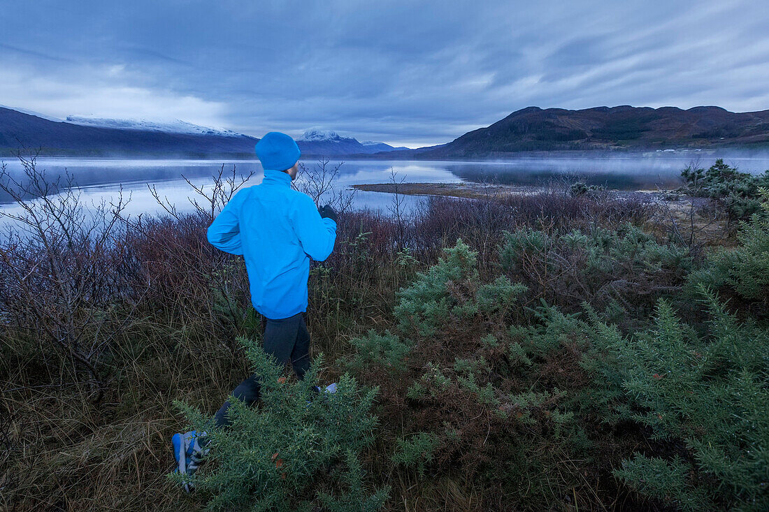 Junger Mann joggt am Loch Maree, Northwest Highlands im Hintergrund, Schottland, Großbritannien