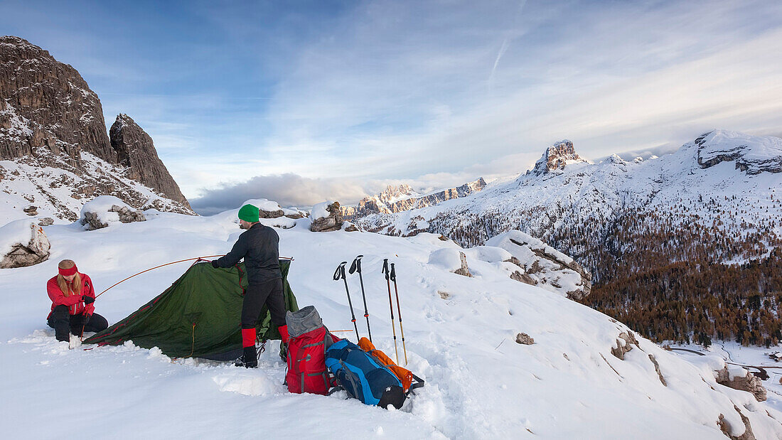 Young couple putting up a tent in snow, Dolomites, Belluno, Veneto, Italy