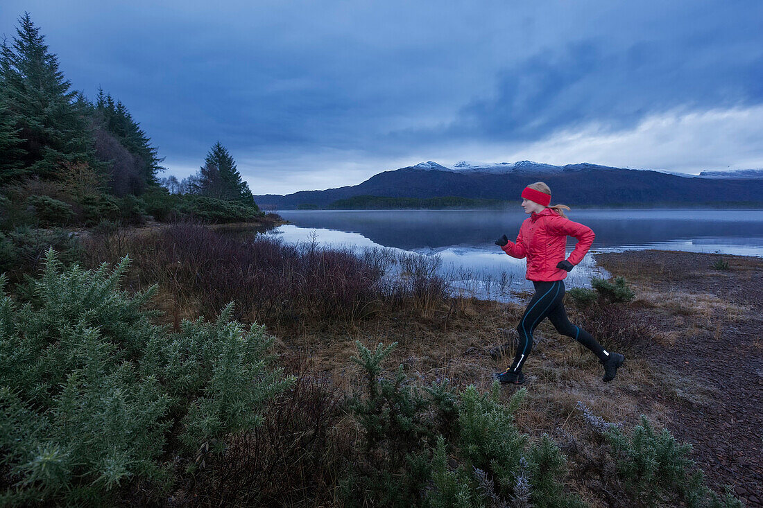 Junge Frau joggt am Loch Maree, Northwest Highlands im Hintergrund, Schottland, Großbritannien