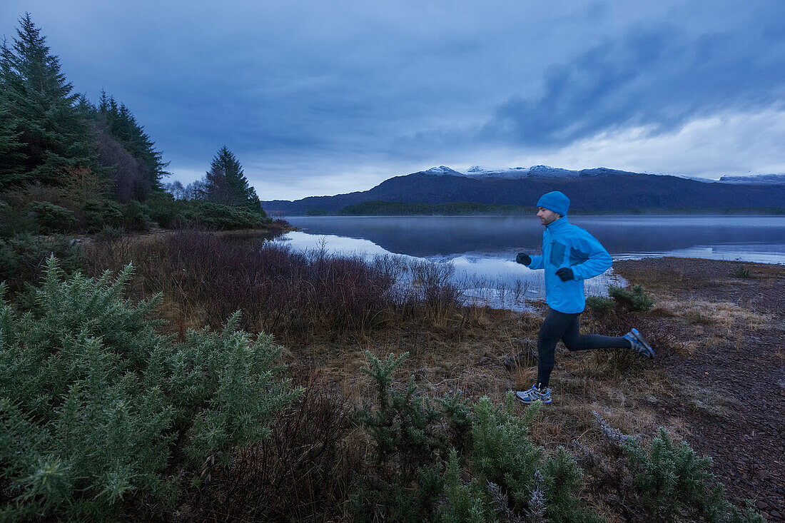 Junger Mann joggt am Loch Maree, Northwest Highlands im Hintergrund, Schottland, Großbritannien