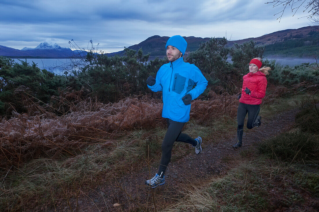 Young couple jogging along Loch Maree, Northwest Highlands in background, Scotland, United Kingdom
