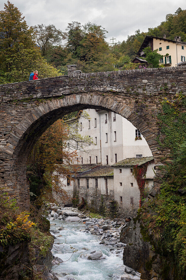 Junge Frau mit Rucksack überquert eine Brücke über den Fluss Mera, Promontogno, Bergell, Kanton Graubünden, Schweiz