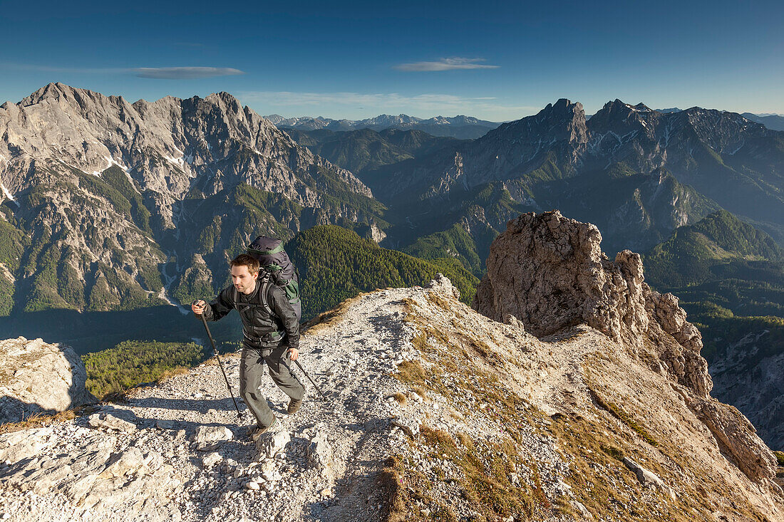 Junger Mann mit Rucksack wandert auf einem steilen Bergpfad am Großen Buchstein, Nationalpark Gesäuse, Hochtor und Admonter Reichensteingruppe im Hintergrund, Ennstaler Alpen, Steiermark, Österreich