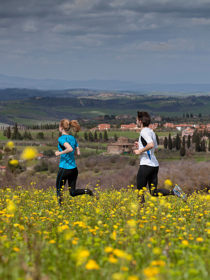 Junges Paar joggt entlang einer Blumenwiese, San Quirico d Orcia, Toskana, Italien