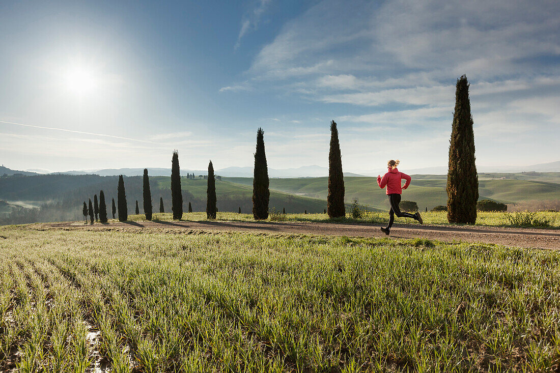 Junge Frau joggt über einen Weg mit Zypressen, Toskana, Italien