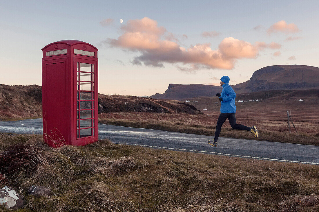 Young man jogging, passing a red booth, Isle of Skye, Trotternish Peninsula, Scotland, United Kingdom