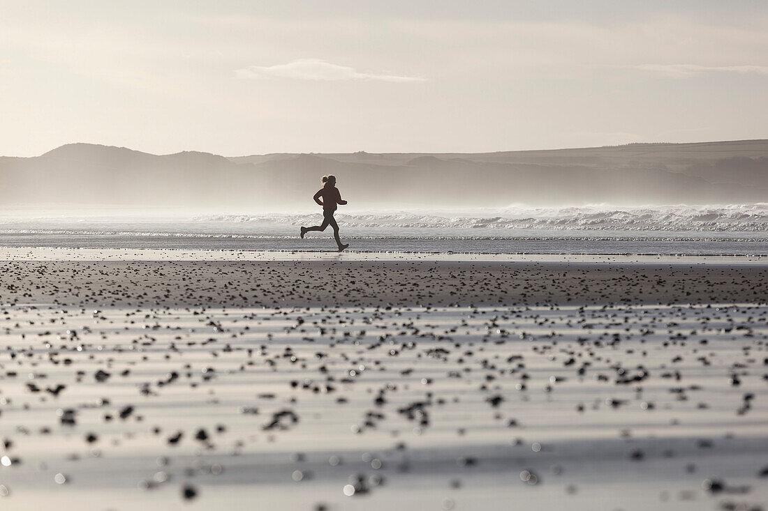 Junge Frau joggt am Strand im Gegenlicht, Dunnet Bay, Caithness, Schottland, Großbritannien