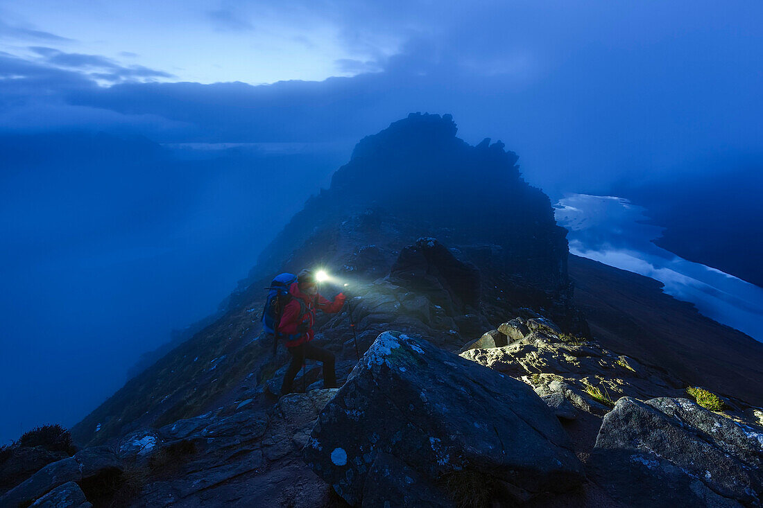 Young woman with headlamp ascending to the summit of Stac Pollaidh at dusk, Assynt, Scotland, United Kingdom