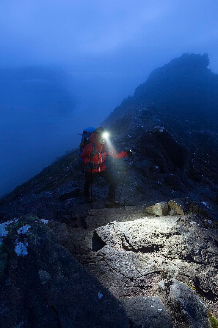 Young woman with headlamp ascending to the summit of Stac Pollaidh at dusk, Assynt, Scotland, United Kingdom